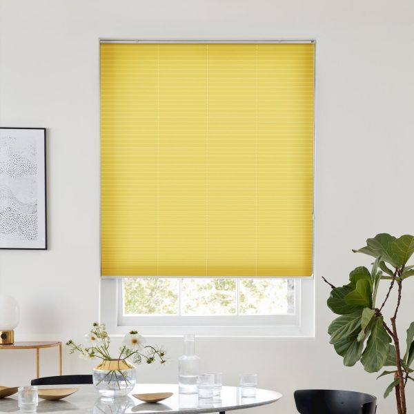 Yellow pleated blind, fully lowered across a window; blocking and softly diffusing daylight in a bright minimalist dining area with round table, vase of flowers, framed art and fiddle‑leaf fig.