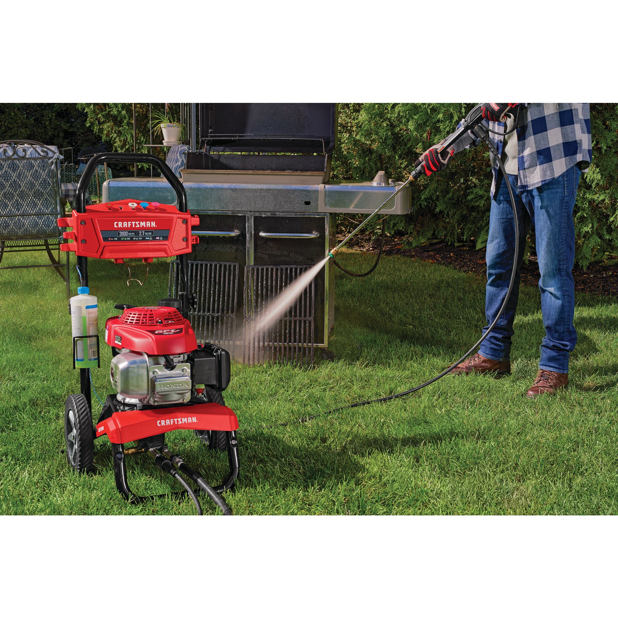 3100 MAX Pounds per Square Inch or 2 and seven tenths MAX Gallons Per Minute Pressure Washer being used by person to wash Bar B Que grills placed outdoors in lawn.