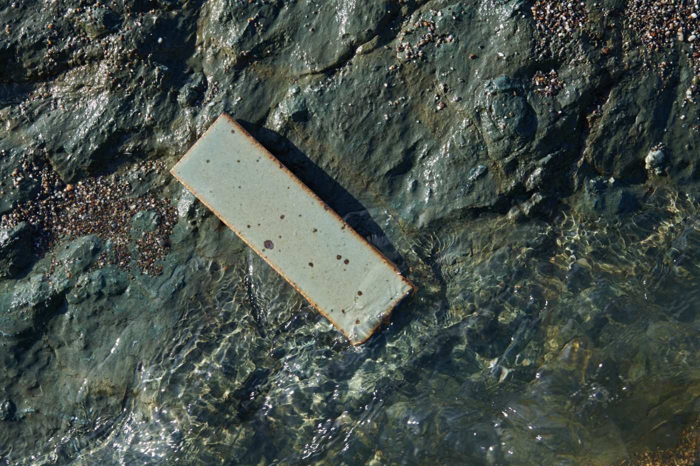 a rectangular tile laying on a rock in the water.