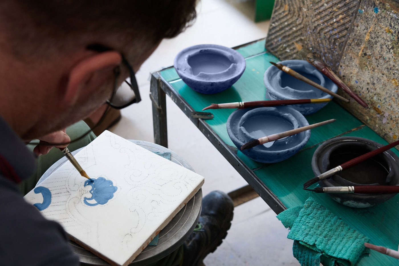 a man hand painted a tile in an art studio.