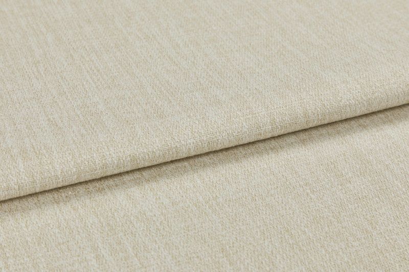 Beige woven upholstery fabric (window dressing absent), folded once with an overlapping edge; close-up shows textured, slightly nubby weave under neutral studio lighting on a flat surface.