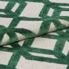 Tufted rug with raised green geometric lattice on a beige ground — folded to show pile and backing — close-up, studio-lit textile sample highlighting textured fibers and overlapping layers.
