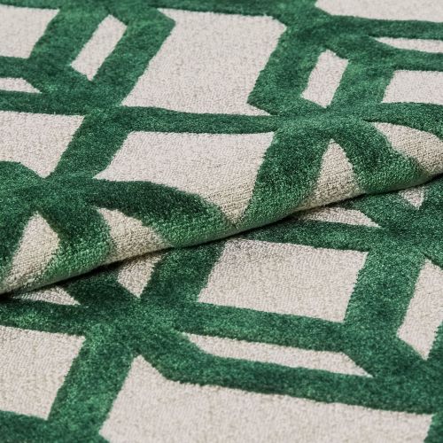 Tufted rug with raised green geometric lattice on a beige ground — folded to show pile and backing — close-up, studio-lit textile sample highlighting textured fibers and overlapping layers.