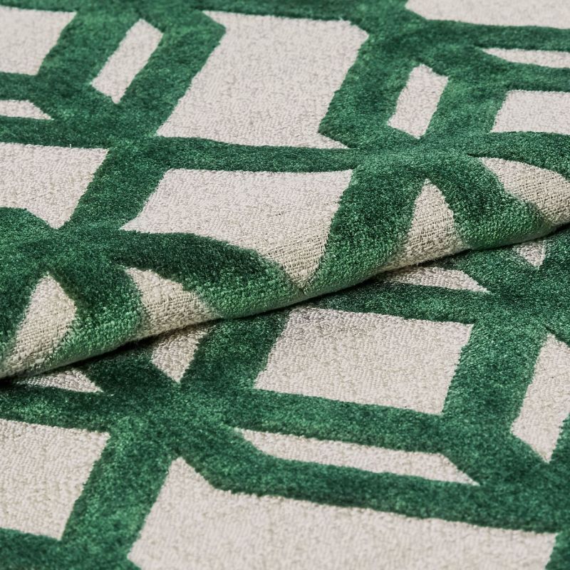 Tufted rug with raised green geometric lattice on a beige ground â€” folded to show pile and backing â€” close-up, studio-lit textile sample highlighting textured fibers and overlapping layers.