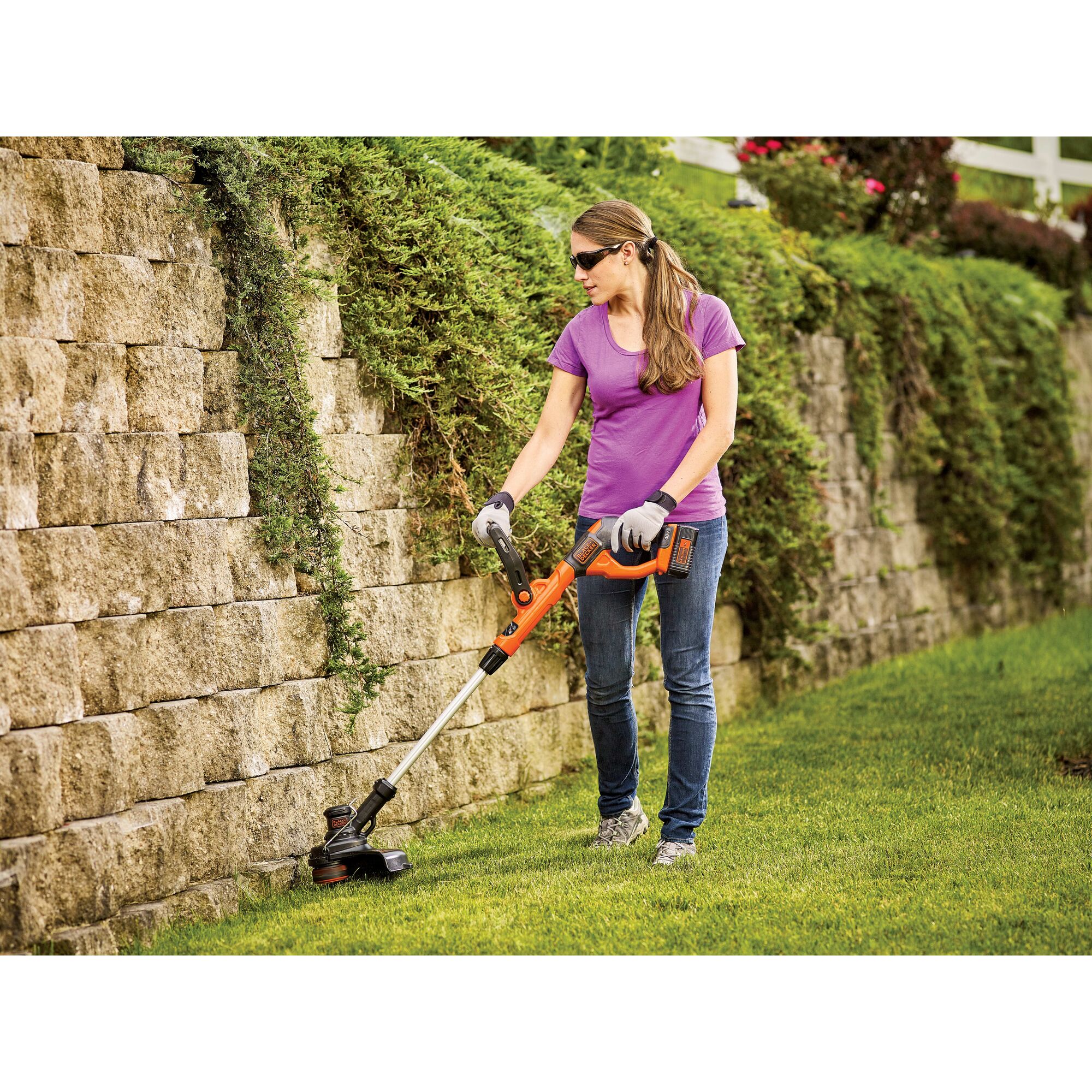 Woman using 40V MAX* Cordless String Trimmer along edge of stone wall.