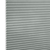 Light-gray pleated cellular (honeycomb) blind, tightly closed with visible hexagonal cells at left edge; filtering/diffusing light, photographed close-up filling the frame against a white background.