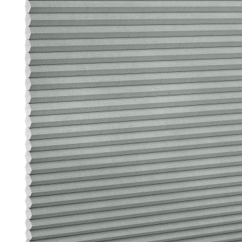 Light-gray pleated cellular (honeycomb) blind, tightly closed with visible hexagonal cells at left edge; filtering/diffusing light, photographed close-up filling the frame against a white background.
