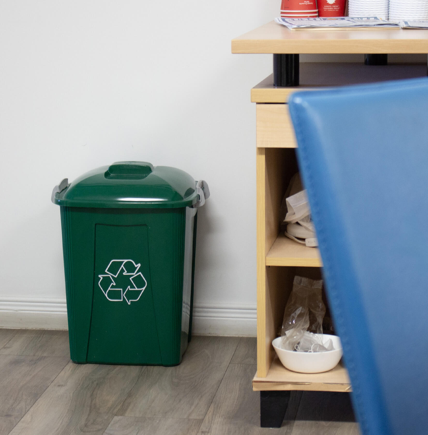 small green plastic recycling bin with locking lid sitting on the floor in an office break room