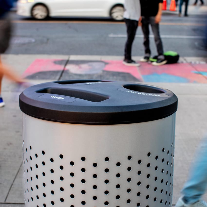 closeup of a metal and plastic multi-stream waste and recycling container outside on a busy city sidewalk