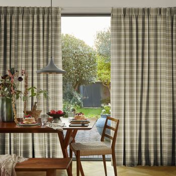 Beige plaid pleated curtains, mostly drawn with a central gap revealing the outside; filtering soft morning light over a wooden dining table set for breakfast, pendant lamp, and garden view.