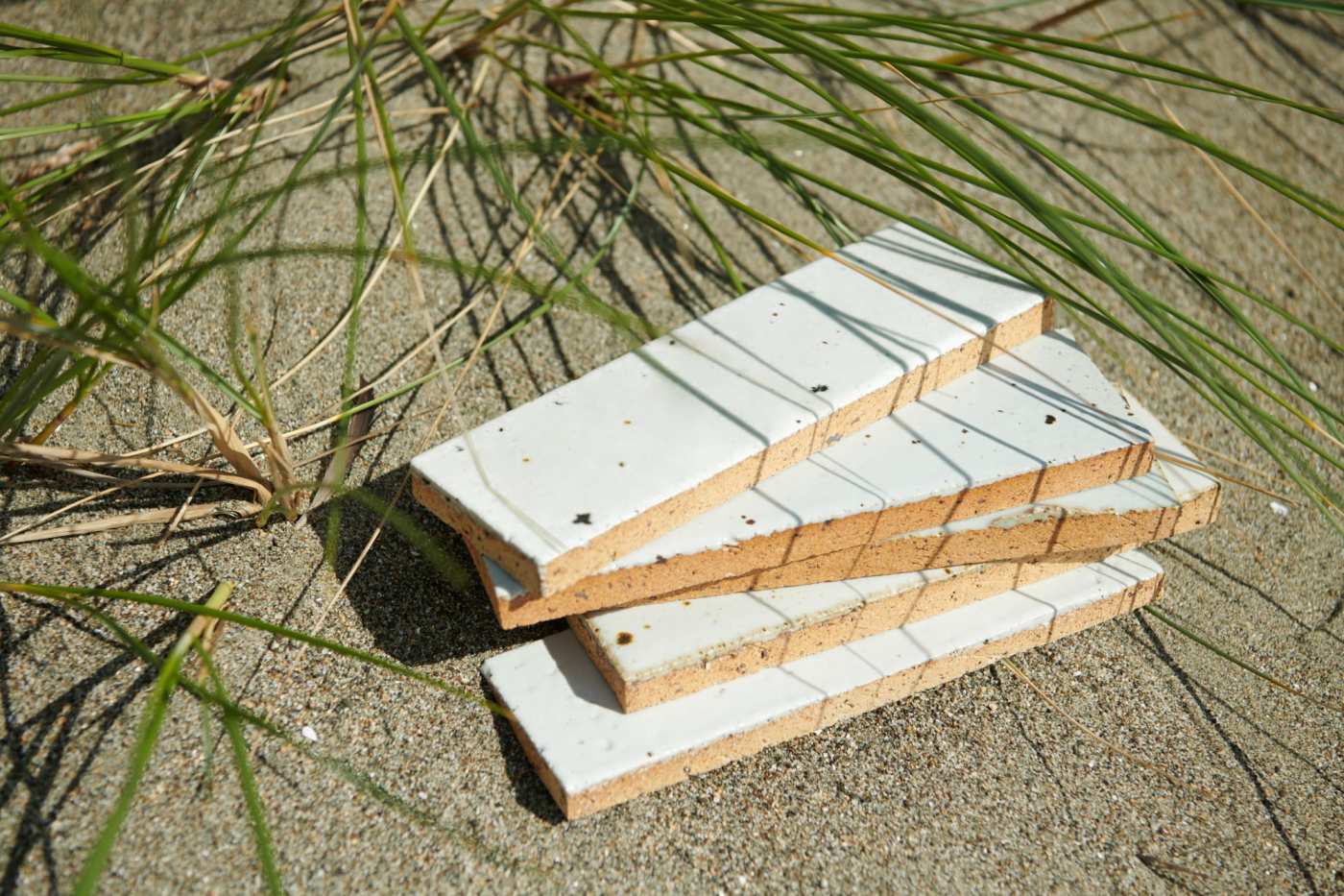 a stack of white rectangle tiles on the sand next to grass.