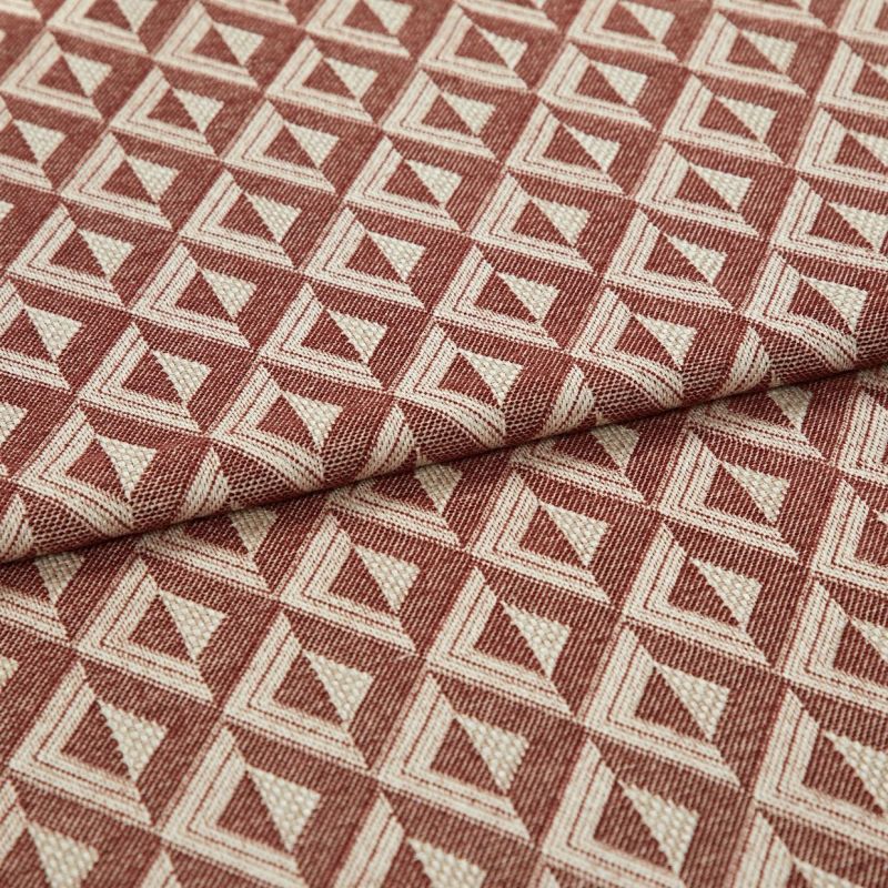 Woven upholstery fabric with repeating terracotta-and-cream triangular motif, folded once across the frame, revealing textured weave and raised pattern; close-up, evenly lit studio shot on neutral surface.