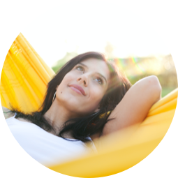 A woman laying in a yellow hammock and looking at the sky.
