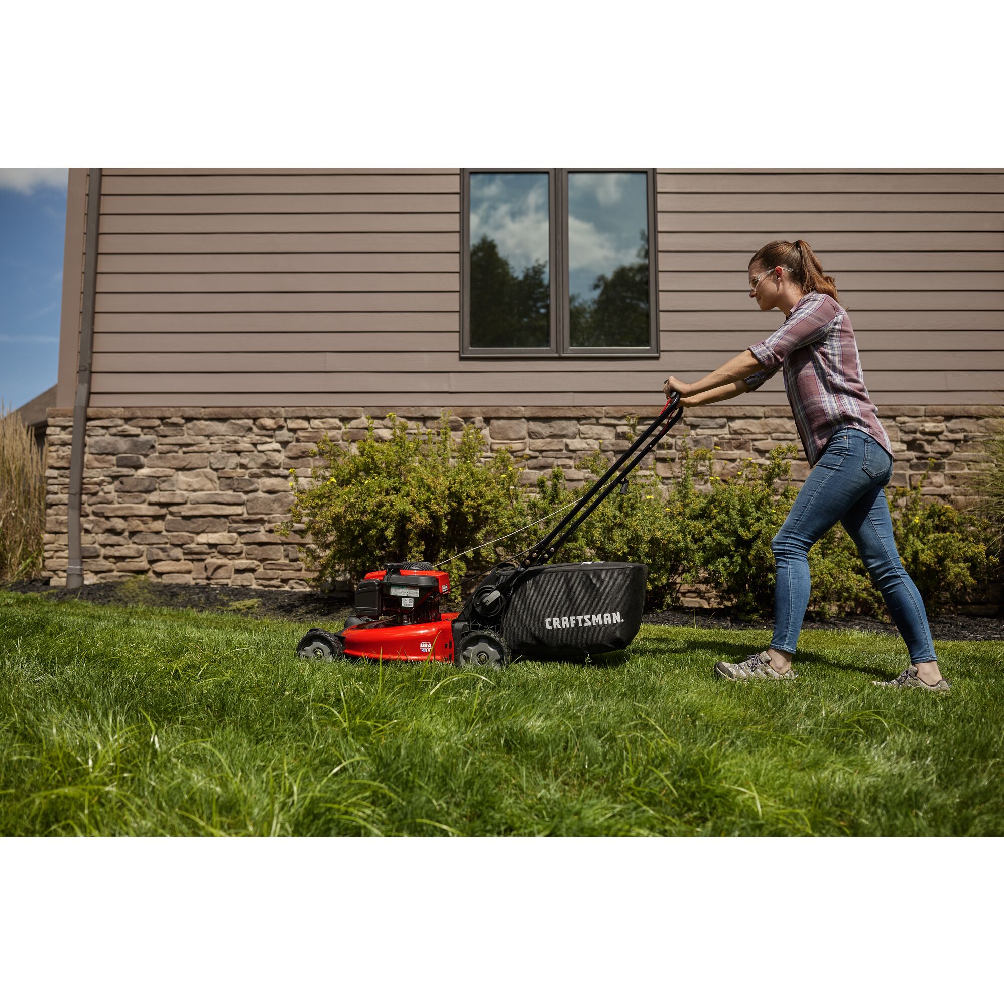 CRAFTSMAN 21-in 150cc Push Mower mowing grass in the backyard in side view in plaid and jeans
