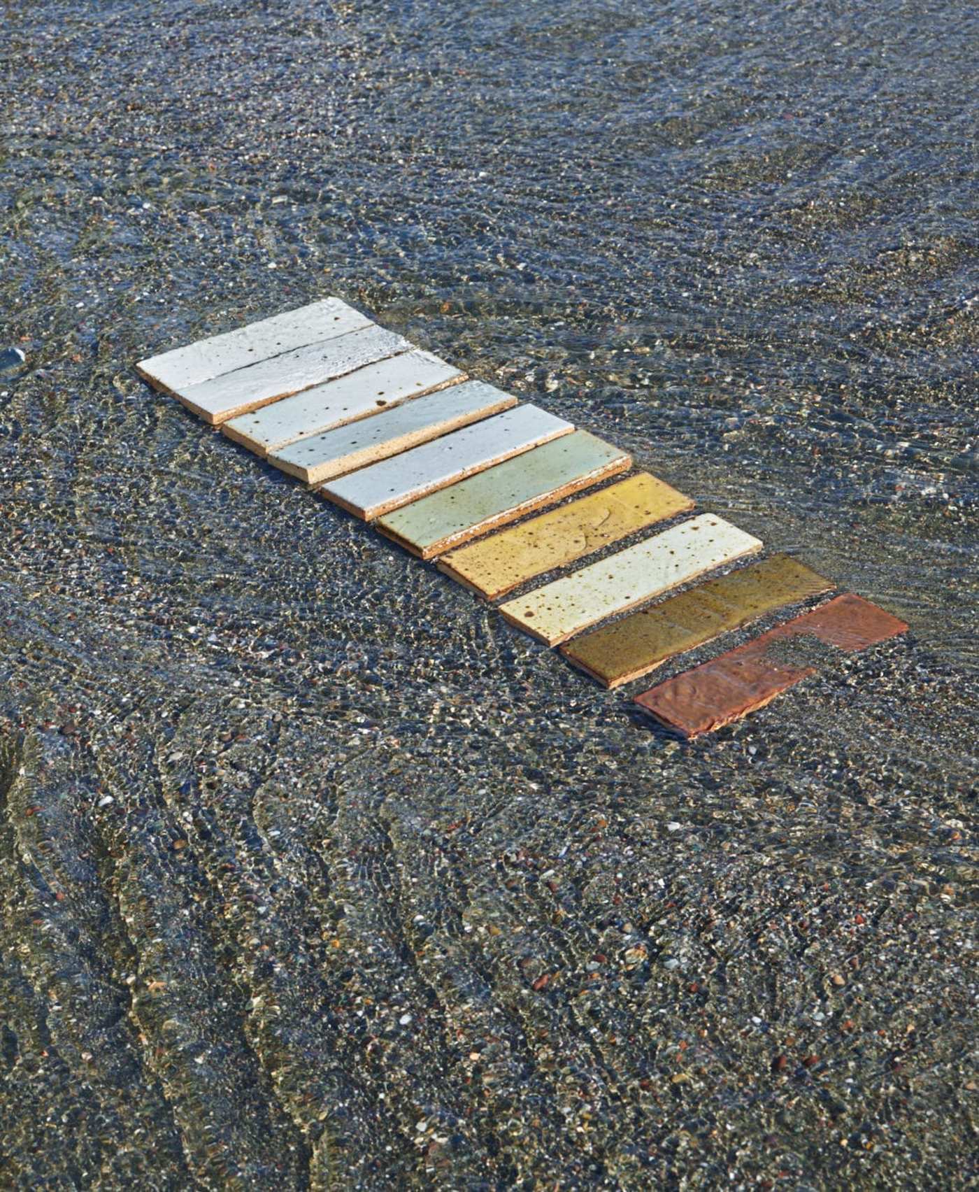 a set of multicolored rectangle tiles spread along the sand at the beach.