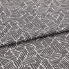 Folded patterned fabric: gray-and-white geometric print of short parallel stripes forming irregular polygons, folded across the middle. Close-up on flat surface with even studio lighting.