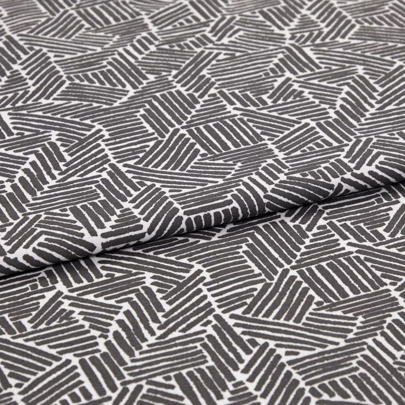 Folded patterned fabric: gray-and-white geometric print of short parallel stripes forming irregular polygons, folded across the middle. Close-up on flat surface with even studio lighting.