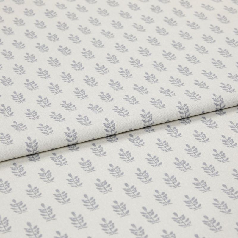 Light-coloured cotton fabric with repeating small grey leaf motifs, folded across the middle, shown in a soft, evenly lit studio close-up.