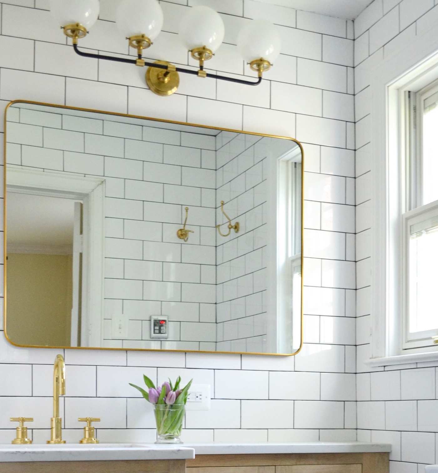 a bathroom with white tile and a gold mirror.