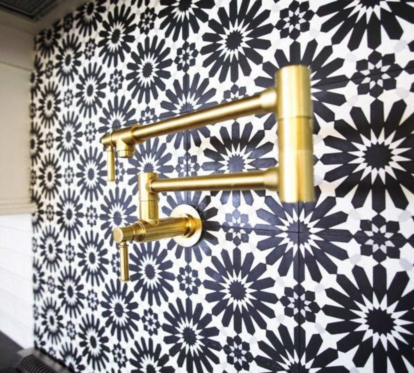 a black and white tiled wall with a gold faucet.