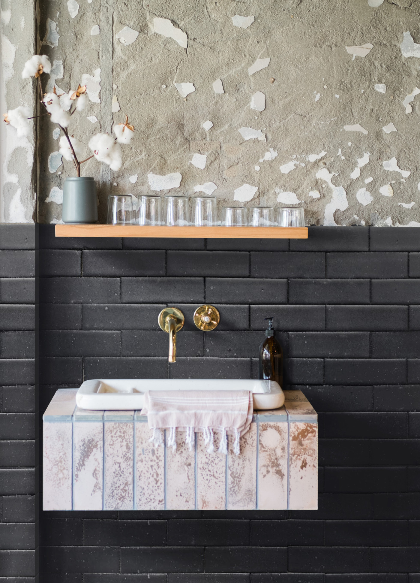 a bathroom with a black tiled wall and a wooden shelf.