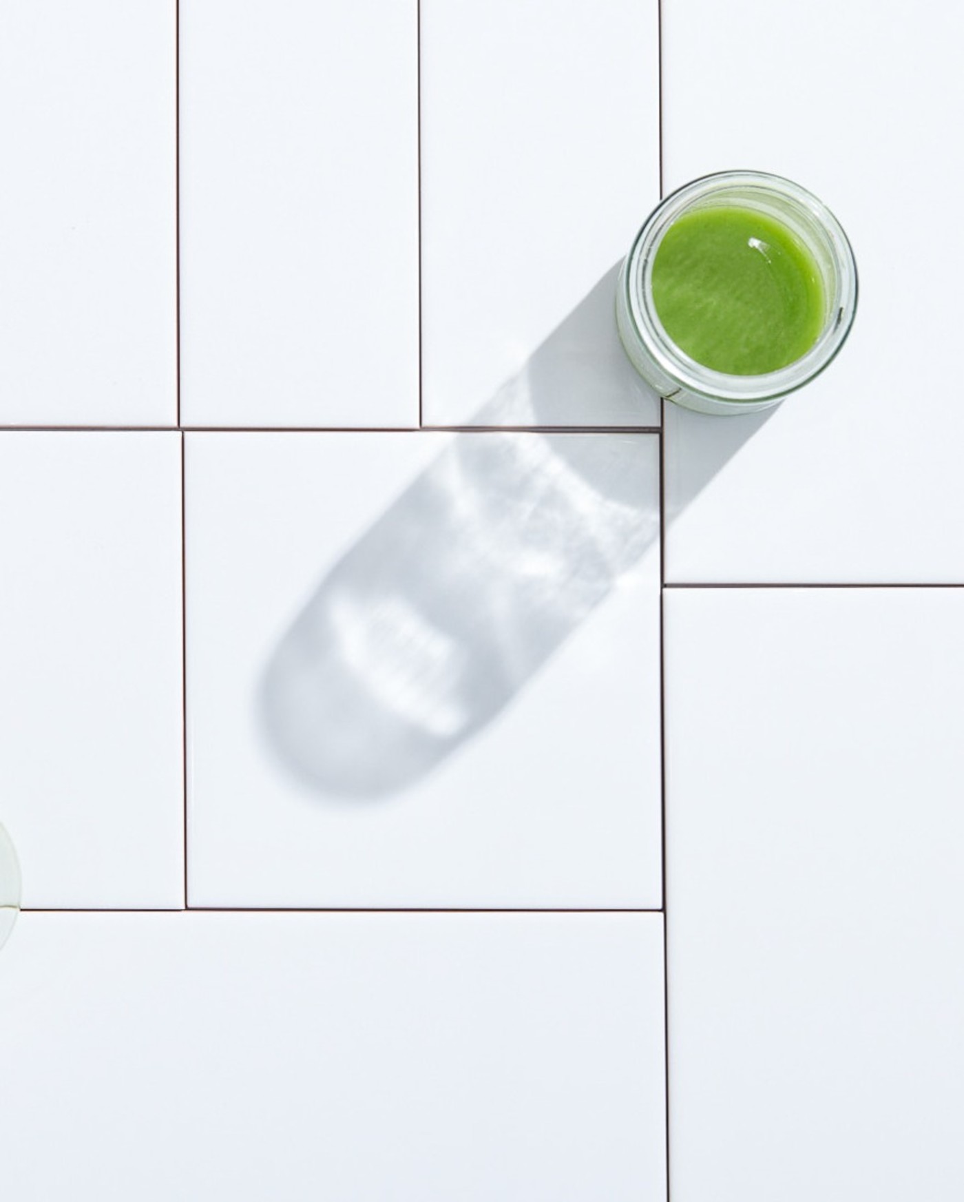 a glass of green juice on a white tiled floor.