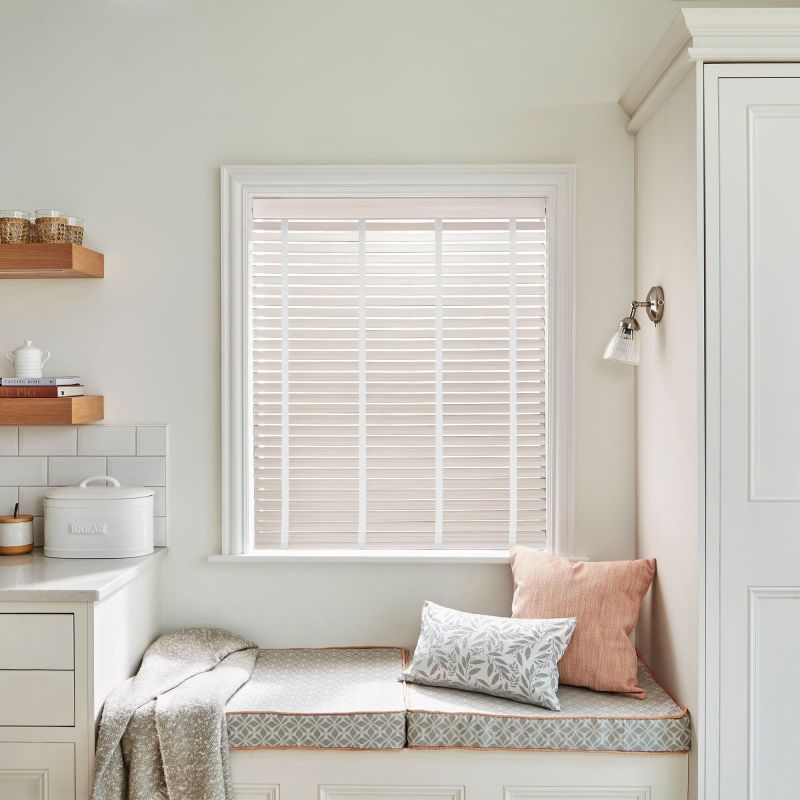 White horizontal slatted blinds within a painted window frame, closed and filtering soft daylight; kitchen nook with cushioned bench, throw and pillows, floating shelves, bread box and neutral decor.

BREAD