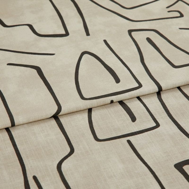 Beige linen-like curtain fabric with bold black abstract line pattern, hem visible; folded into a horizontal pleat; close-up in soft, neutral lighting showing fabric texture.