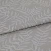 Beige-gray woven fabric with raised white botanical leaf pattern, folded once and layered, displaying texture and subtle sheen; close-up on textile surface under soft, neutral lighting.