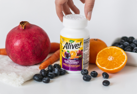 A bottle of Alive Once Daily Women’s Ultra Potency Multivitamin sitting on a white surface surrounded by fruits and vegetables.