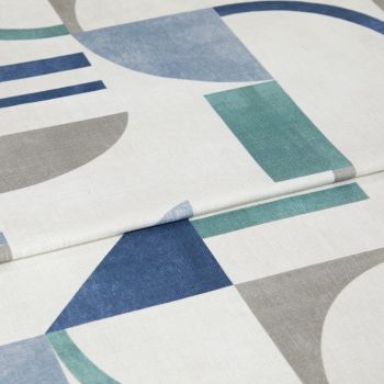 Roman blind with white background and blue, teal, and gray geometric shapes, folded in horizontal pleats; fabric lies flat, showing printed semicircles, rectangles and triangles in soft indoor lighting.