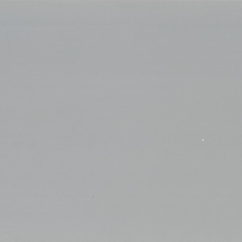 Large smooth matte gray surface with scattered tiny white specks; uniformly lit and stationary; fills frame, suggesting a neutral wall or overcast sky with soft ambient lighting.