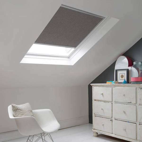 Room with white eaves wall, dark blue-grey wall to right with a shabby chic white drawer unit, a contemporary white chair, white painted floorboards and a skylight blind in mid slate grey.