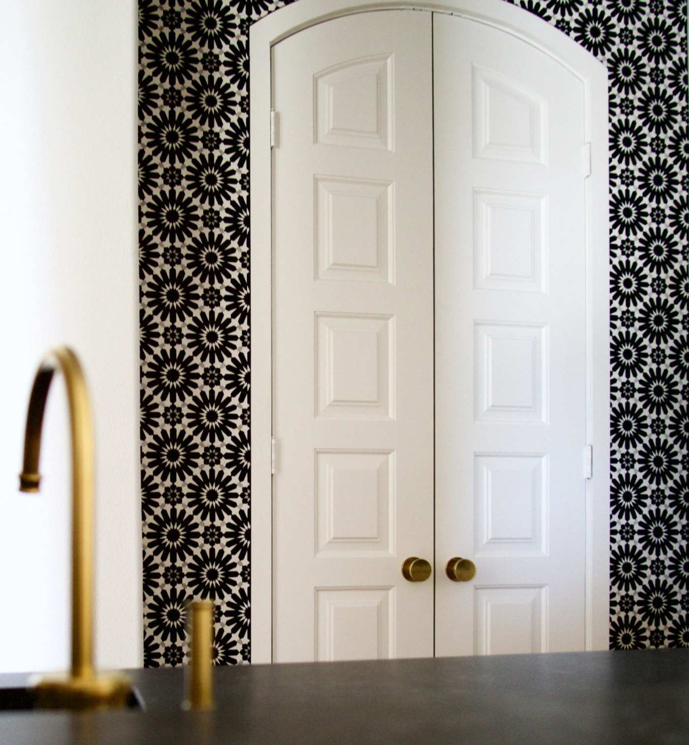 a black and white tiled doorway to a kitchen with a gold faucet.