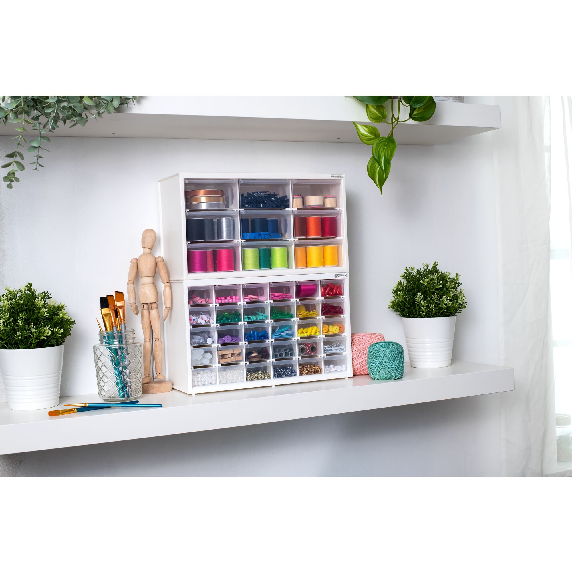 Two BLACK+DECKER material bins filled with various colorful crafting materials stacked on top of each other sitting on a shelf