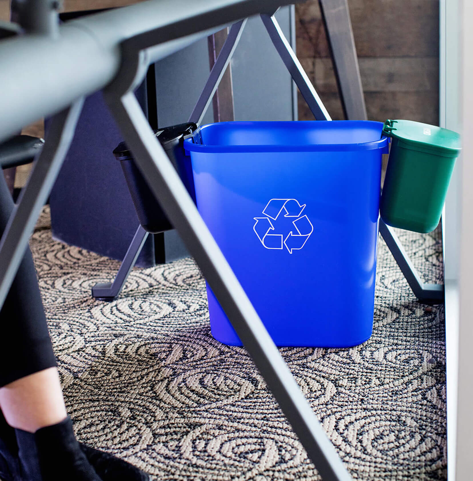 blue recycling bin with two hanging waste and organics collection bins on each side sitting under a modern desk in an office