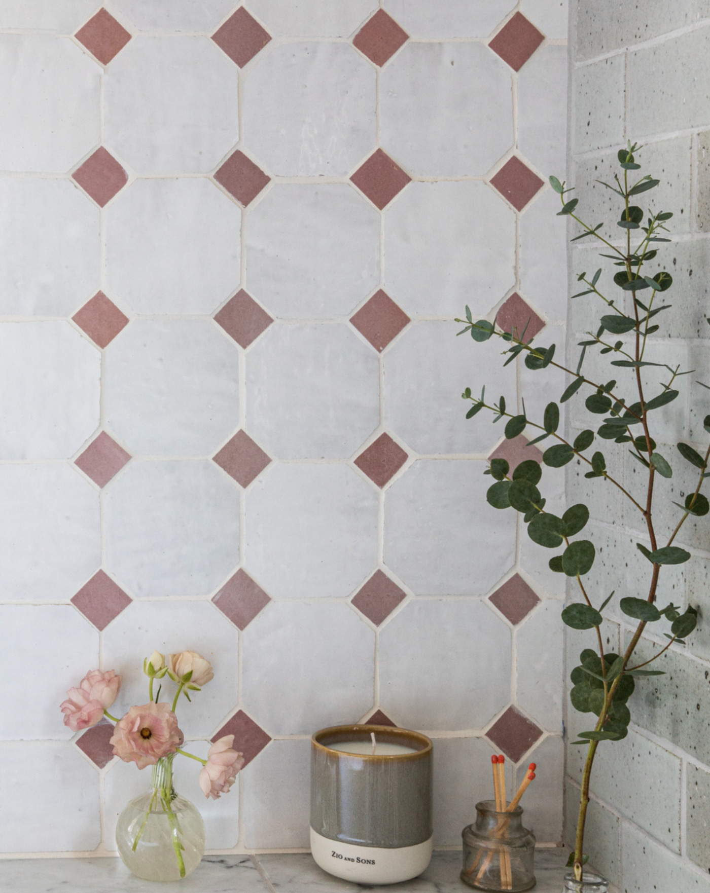 a pink and white tiled wall behind a counter with vase and flowers.