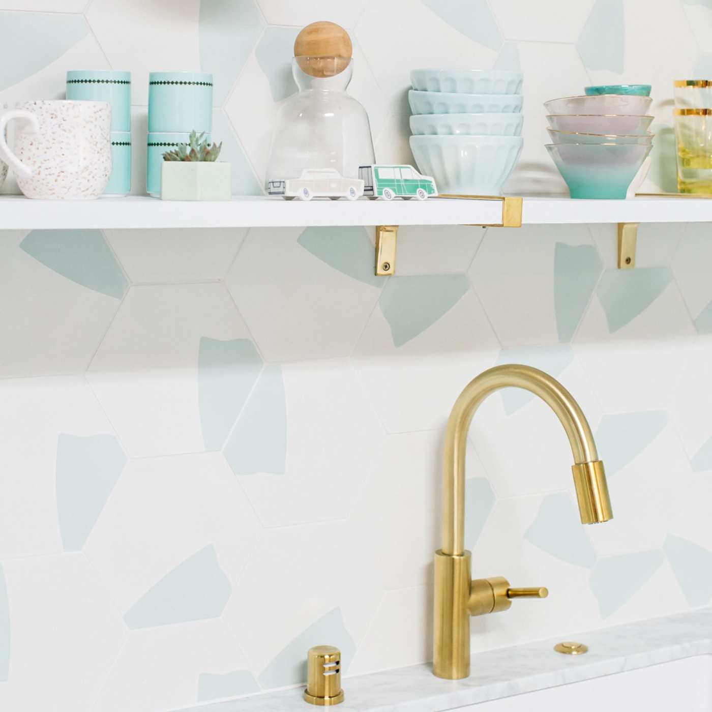 a kitchen with a gold faucet and a blue and white tiled sink backsplash.