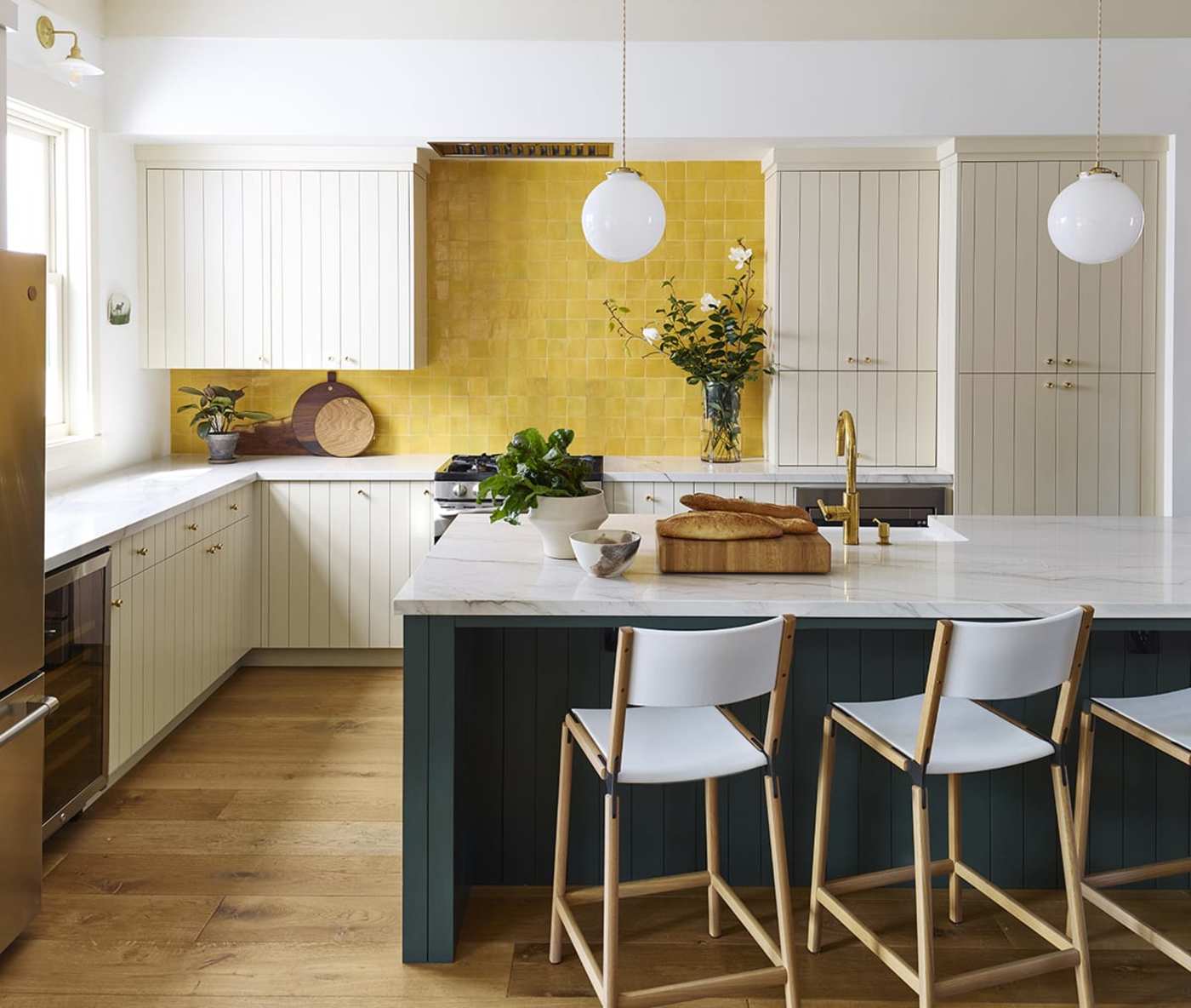 a kitchen with yellow tile backsplash, white cabinets and stools.