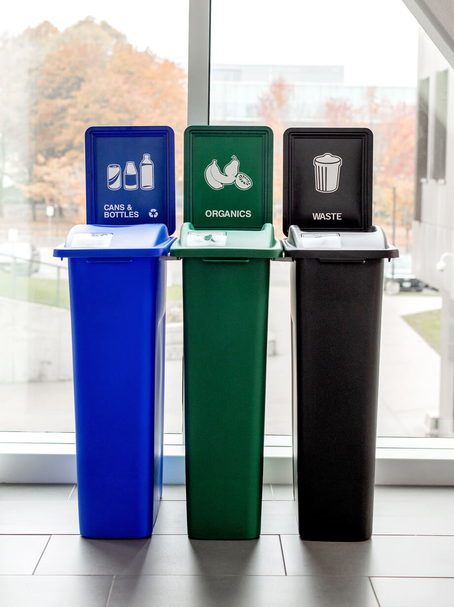 triple station plastic waste recycling and organics bins color coded for optimum waste diversion in a college campus hallway