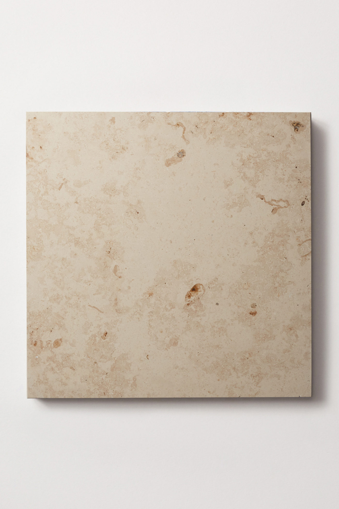 a square limestone tile on a white surface.