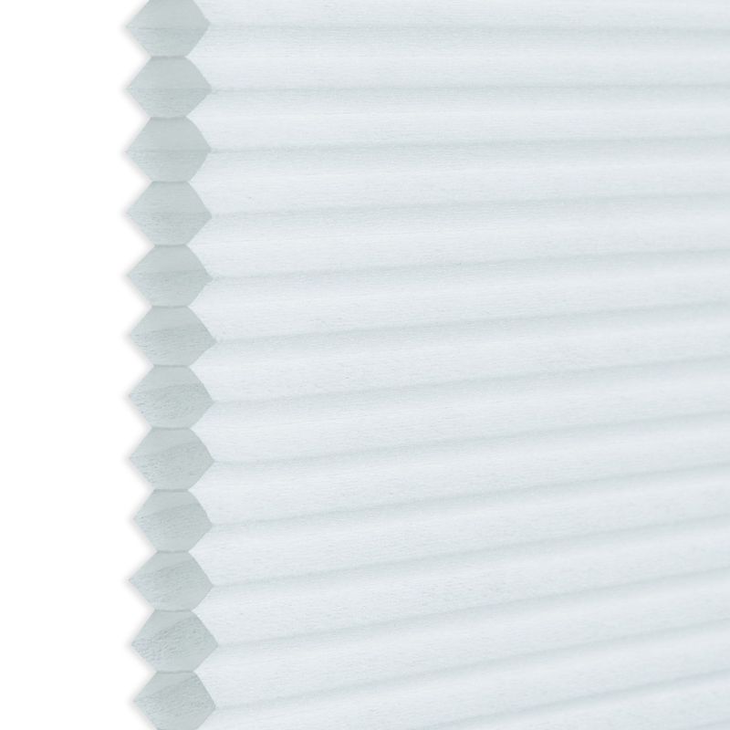 White honeycomb (cellular) blind, hexagonal pleats visible along the left edge; closed and diffusing light; photographed close-up against a neutral background, showing even soft daylight and subtle texture.