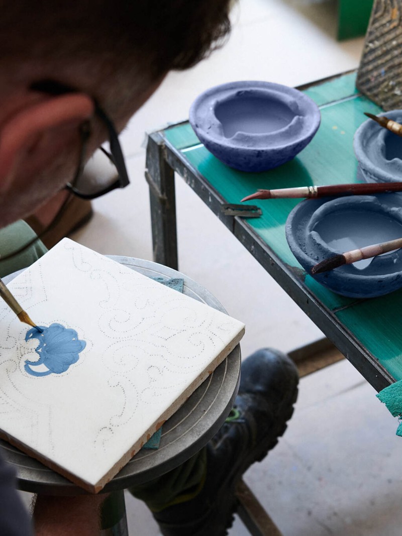 a man hand painting a tile in a workshop.