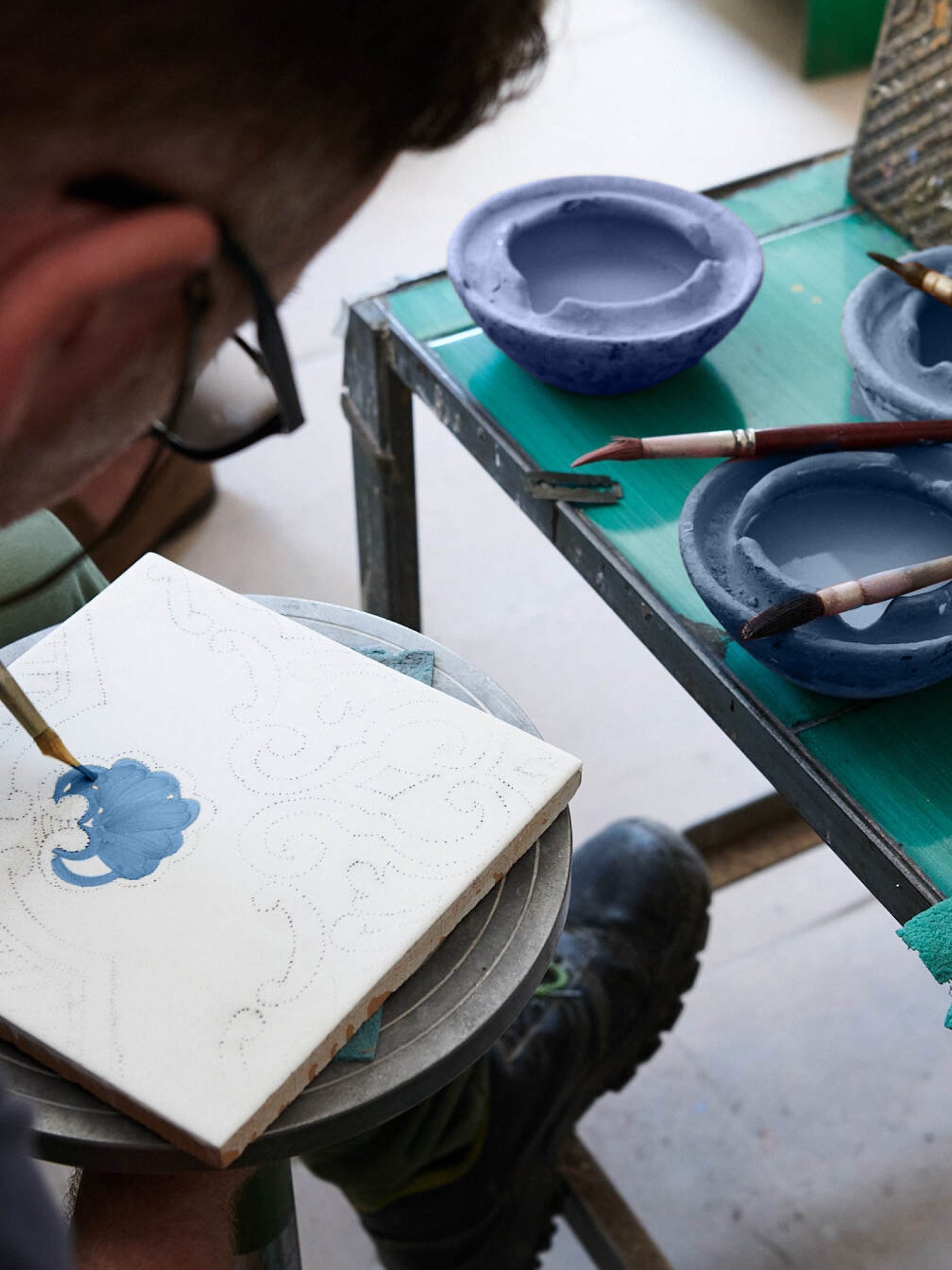 a man is painting a tile in an art workshop.