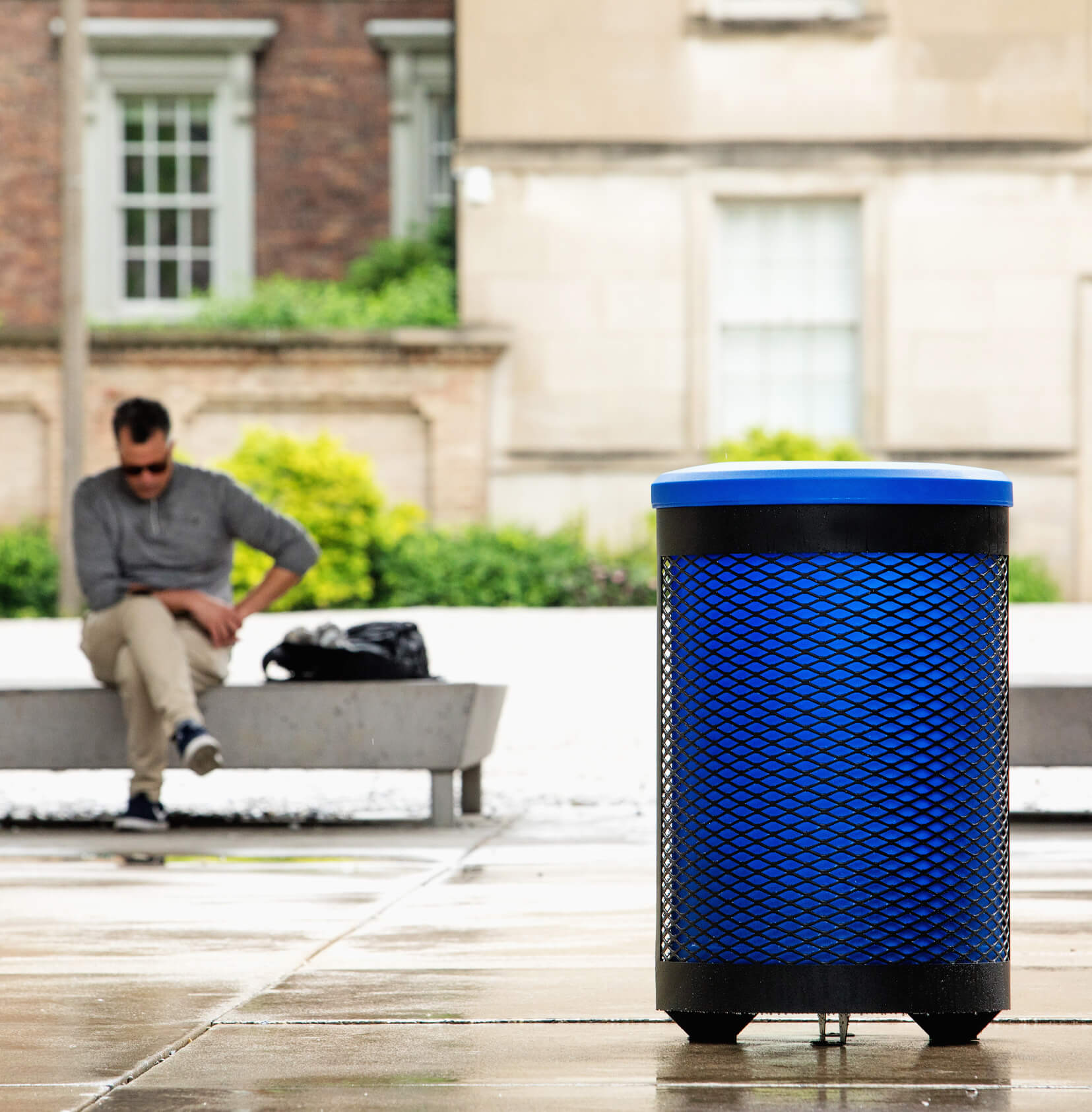 Metal body outdoor recycling bin with plastic blue liner and lid to help improve collection sitting outside a corporate office