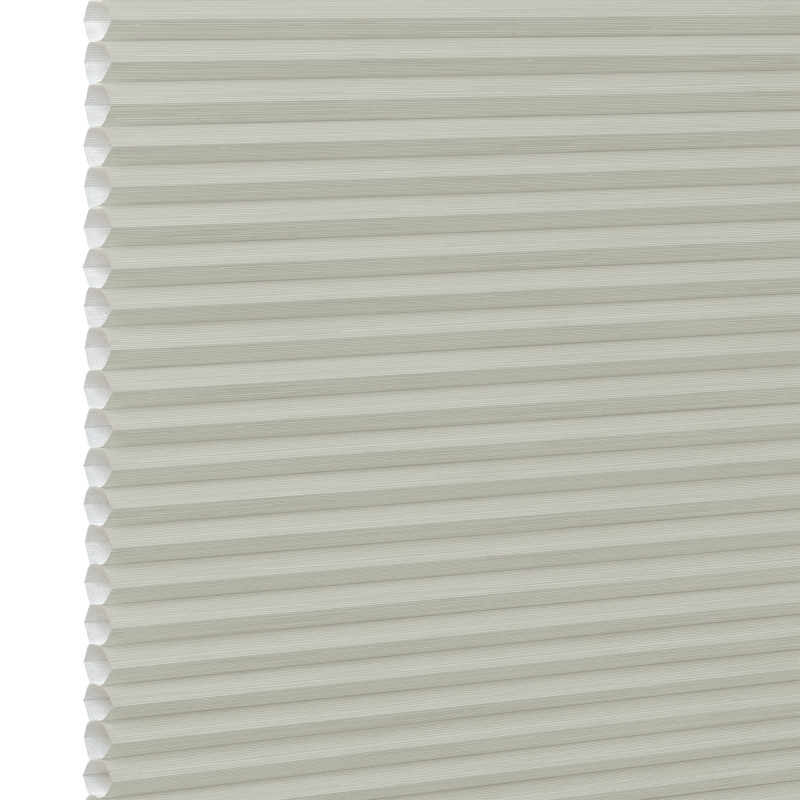 Cream cellular (honeycomb) window blind, fully lowered with visible hexagonal pleats at the left edge; closed and diffusing light; close-up against a plain white background with soft lighting.