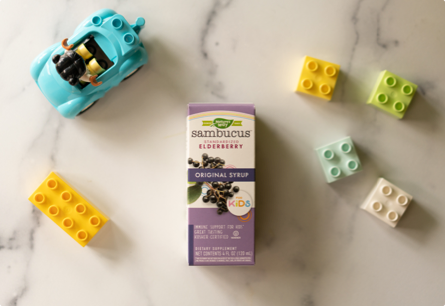 A package of Sambucus Original Syrup for Kids next to a toy car and a few blocks.