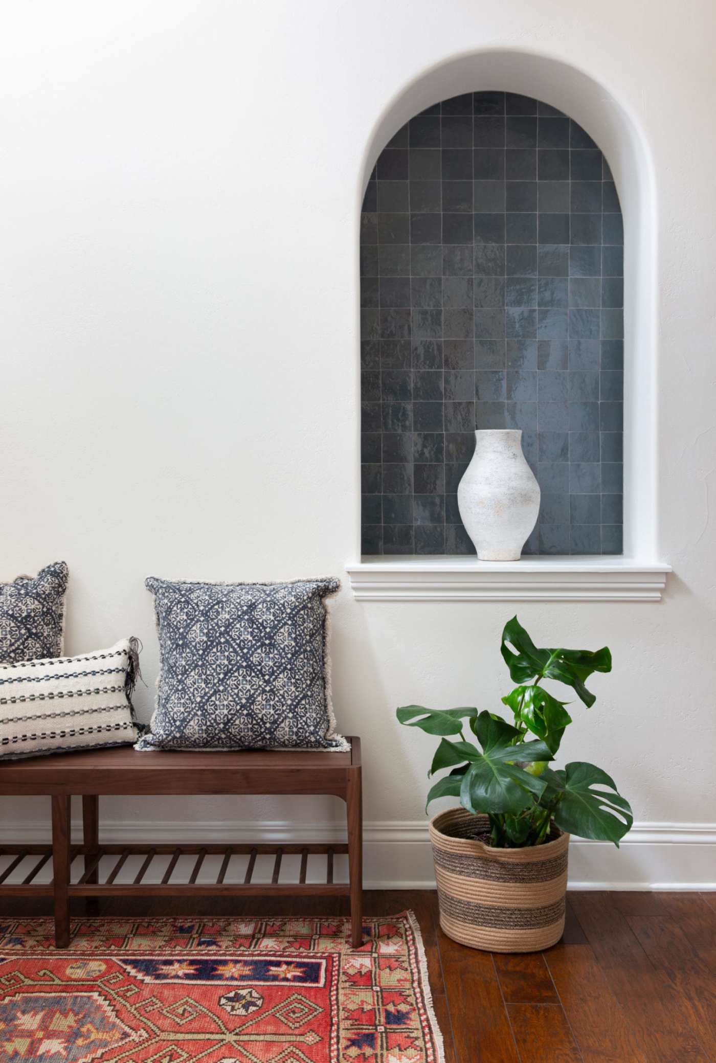 an arched, blue-tiled niche in a room with a bench and a potted plant.