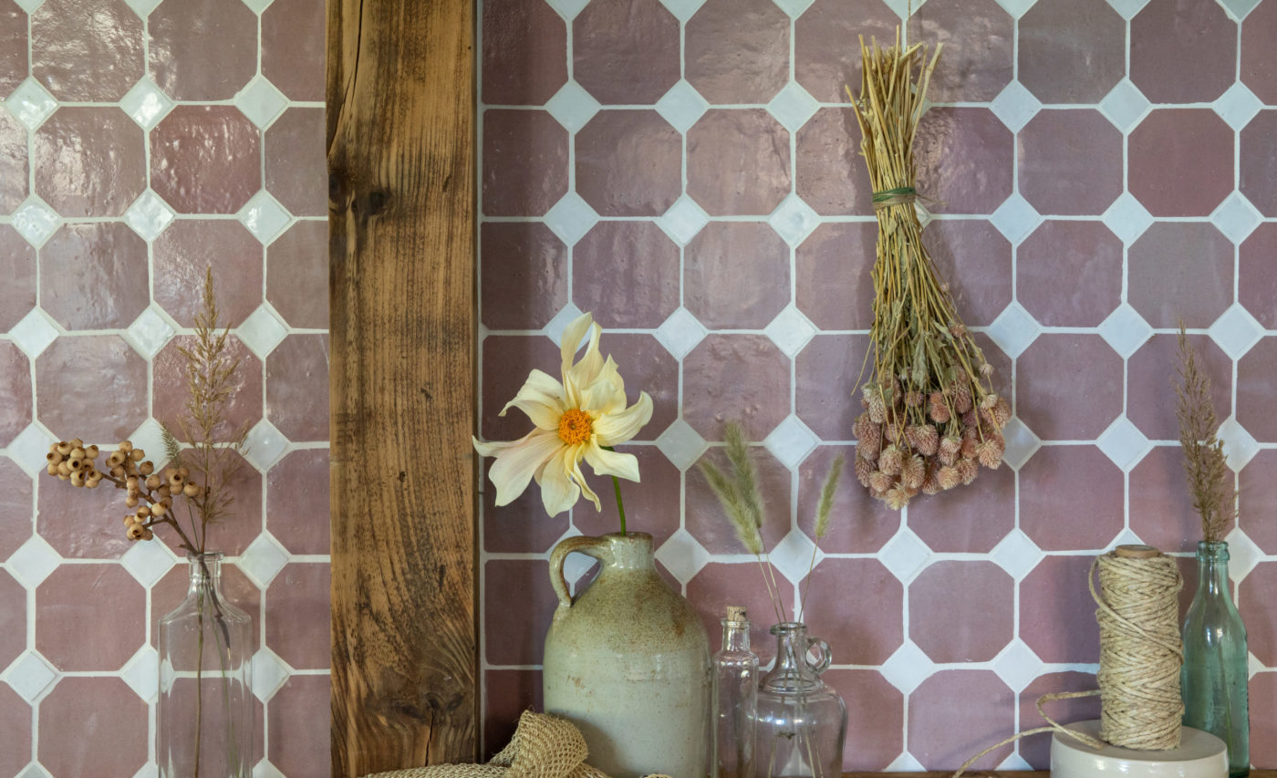 a pink tiled wall with dried flowers and a flower vase.