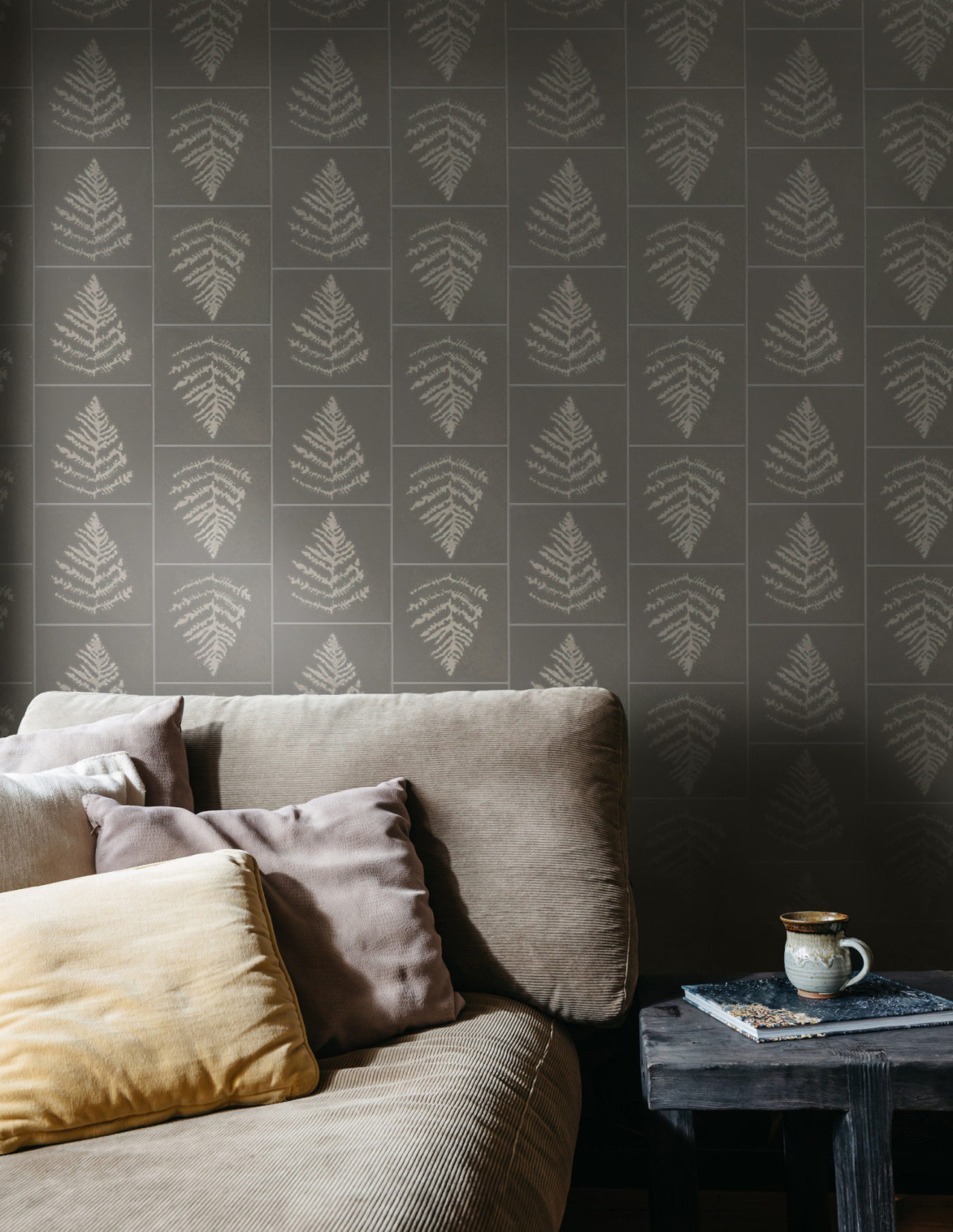 a living room with a couch, coffee table, and grey tile walls with fern leaf prints.